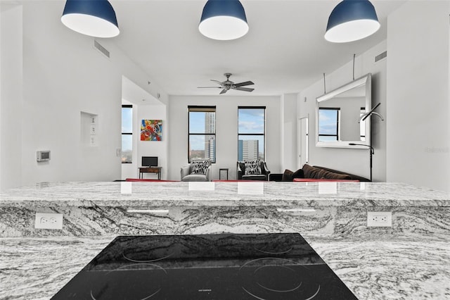 kitchen featuring ceiling fan, black stovetop, light stone counters, and pendant lighting