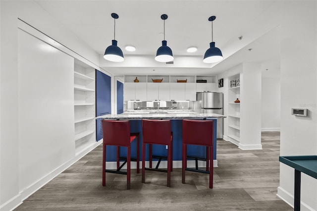 kitchen featuring built in shelves, a breakfast bar, a kitchen island with sink, white cabinets, and stainless steel fridge