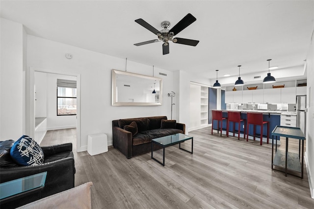 living room featuring ceiling fan, light wood-type flooring, and built in features