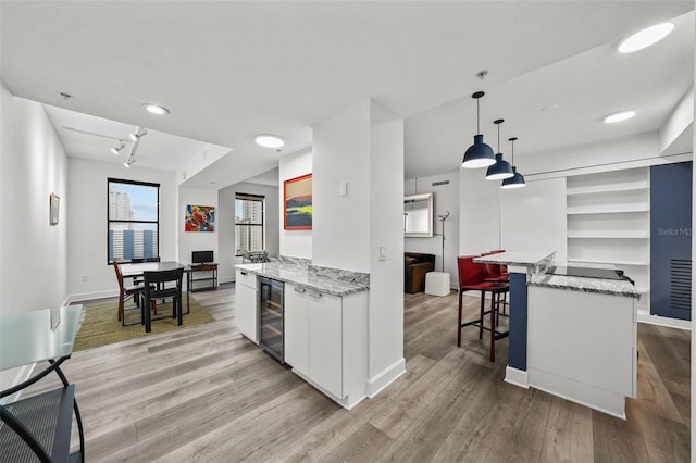 kitchen with wine cooler, light hardwood / wood-style floors, pendant lighting, white cabinets, and light stone counters