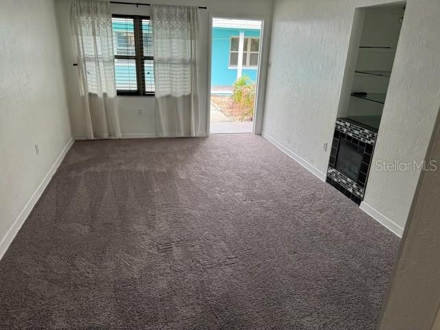 unfurnished living room with a tiled fireplace and carpet floors