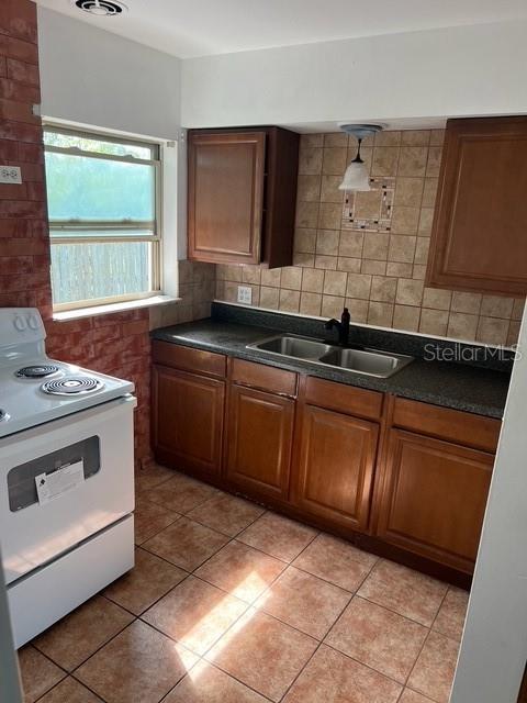 kitchen featuring sink, tasteful backsplash, white range with electric cooktop, pendant lighting, and light tile patterned flooring