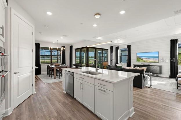 kitchen featuring dishwasher, white cabinets, sink, light wood-type flooring, and an island with sink