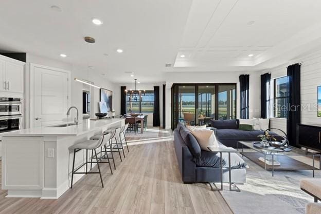 living room with a tray ceiling, sink, and light hardwood / wood-style floors