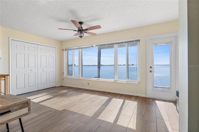 unfurnished bedroom with ceiling fan, a water view, a closet, and a textured ceiling