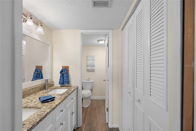 bathroom featuring toilet, wood-type flooring, vanity, and a textured ceiling