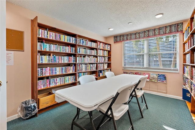 carpeted office space featuring baseboards, a textured ceiling, and wall of books