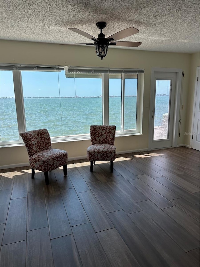 unfurnished room with dark wood-type flooring, baseboards, a water view, a textured ceiling, and a ceiling fan