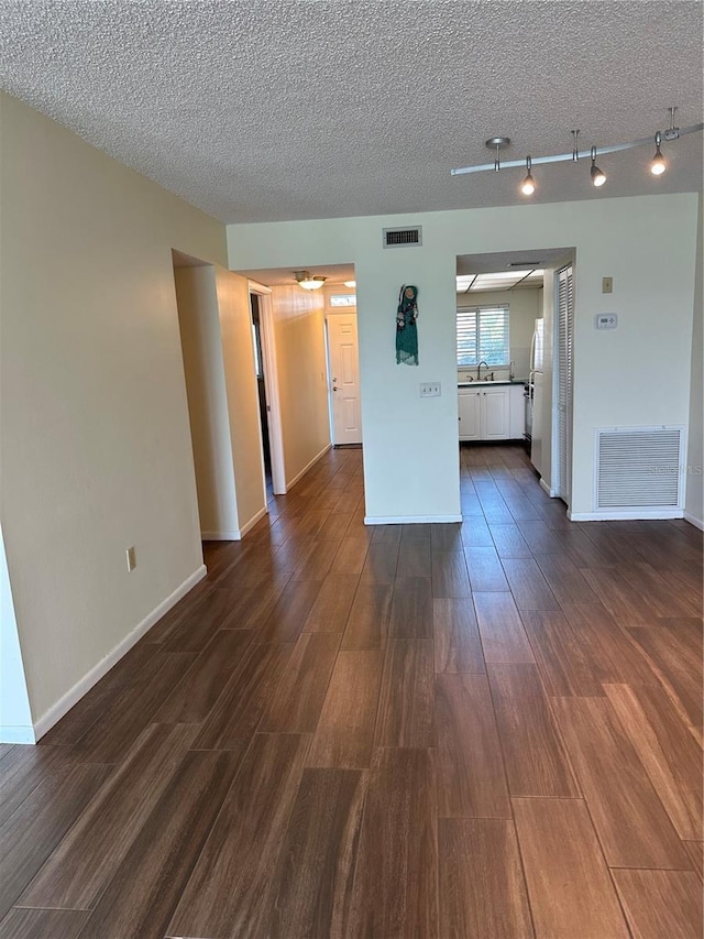 unfurnished living room with visible vents, a textured ceiling, and dark wood-style floors