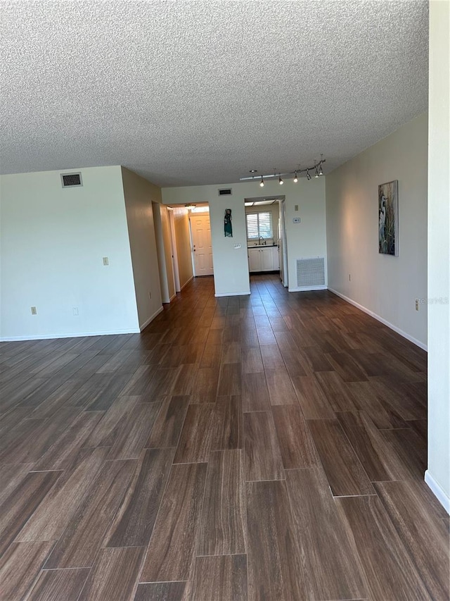 unfurnished living room with visible vents, baseboards, a textured ceiling, and dark wood finished floors