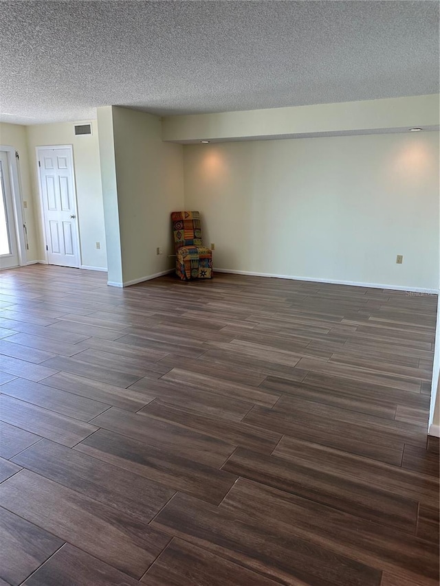 empty room featuring visible vents, dark wood-type flooring, a textured ceiling, and baseboards