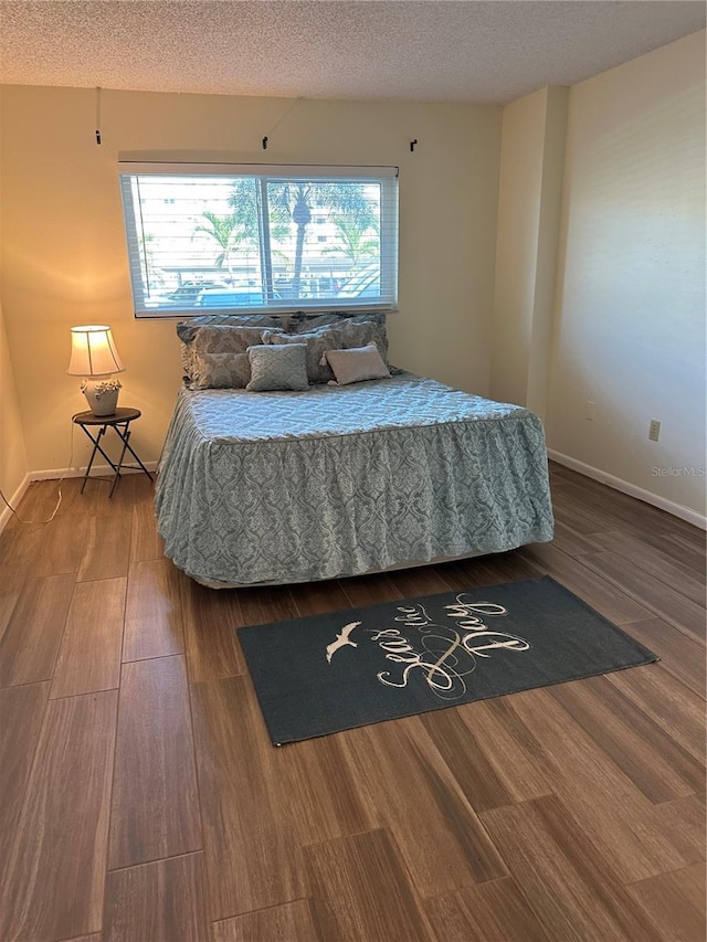 bedroom with baseboards, a textured ceiling, and wood finished floors