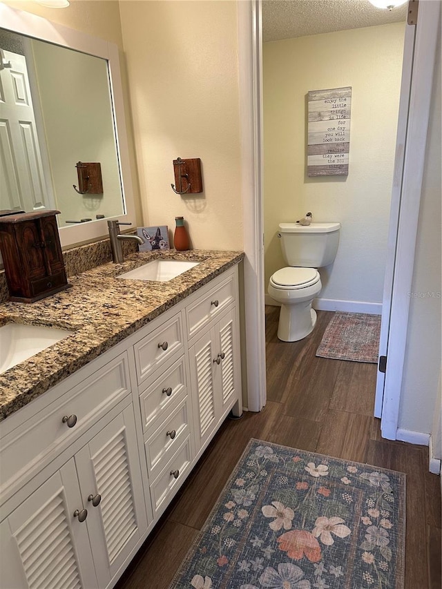 bathroom with toilet, double vanity, wood finished floors, a textured ceiling, and a sink