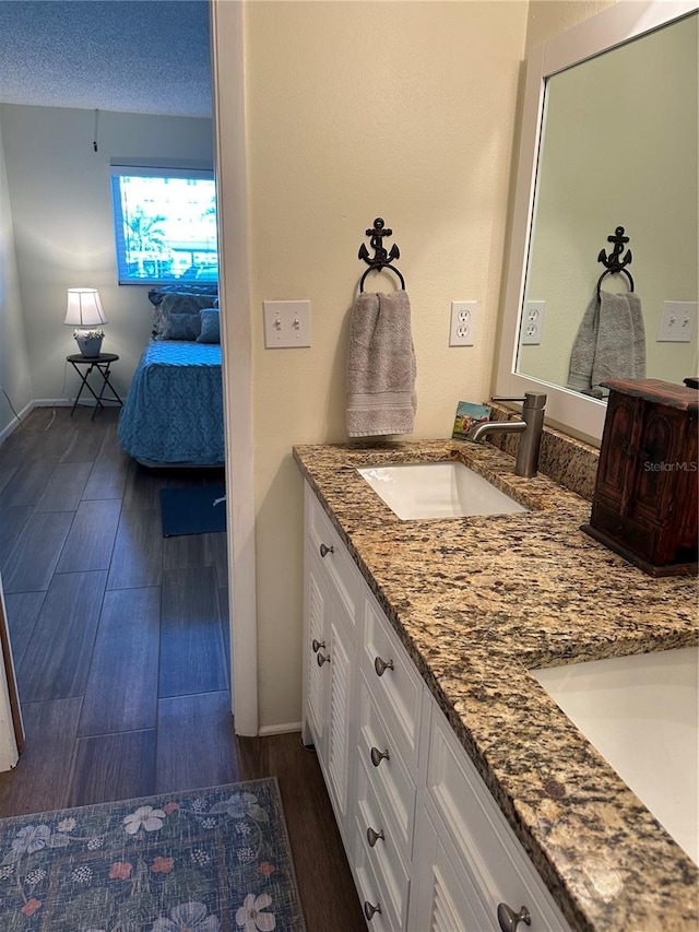 ensuite bathroom featuring a sink, a textured ceiling, wood finished floors, double vanity, and baseboards