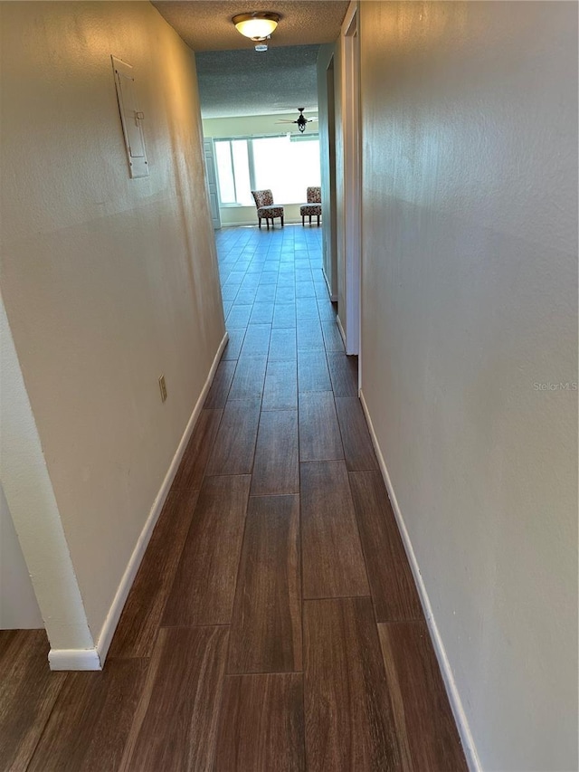 corridor featuring baseboards, dark wood-type flooring, and a textured ceiling