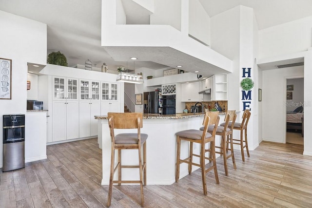 kitchen with kitchen peninsula, light wood-type flooring, black fridge, white cabinets, and a high ceiling