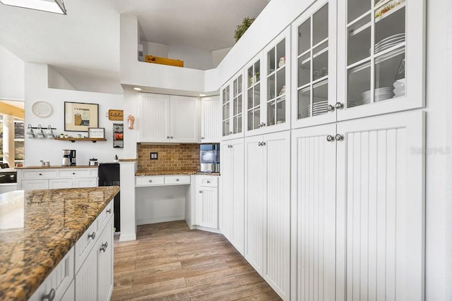 kitchen featuring tasteful backsplash, white cabinetry, dark stone counters, and light hardwood / wood-style flooring