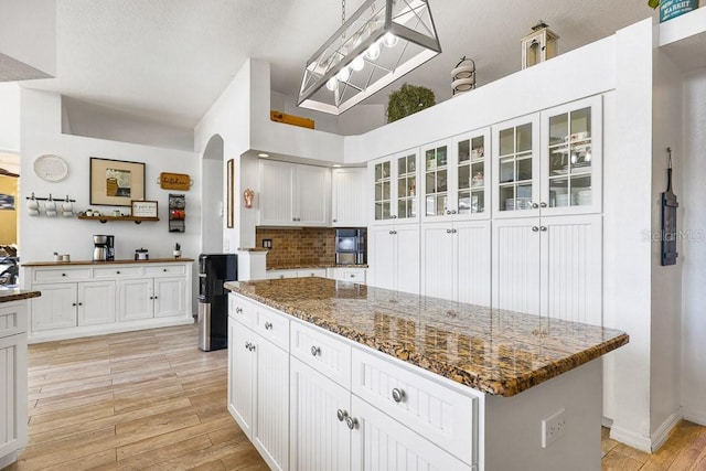 kitchen with dark stone counters, white cabinets, a high ceiling, a center island, and light hardwood / wood-style floors