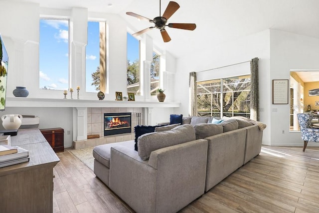 living room with a tile fireplace, ceiling fan, light hardwood / wood-style flooring, and high vaulted ceiling