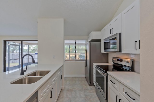 kitchen with sink, stainless steel appliances, white cabinets, vaulted ceiling, and light tile patterned flooring