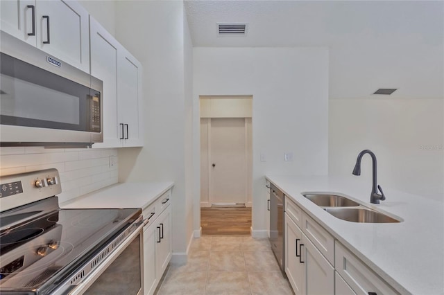 kitchen featuring white cabinets, decorative backsplash, light tile patterned flooring, and appliances with stainless steel finishes