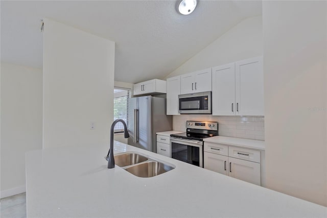 kitchen featuring sink, tasteful backsplash, lofted ceiling, white cabinets, and appliances with stainless steel finishes