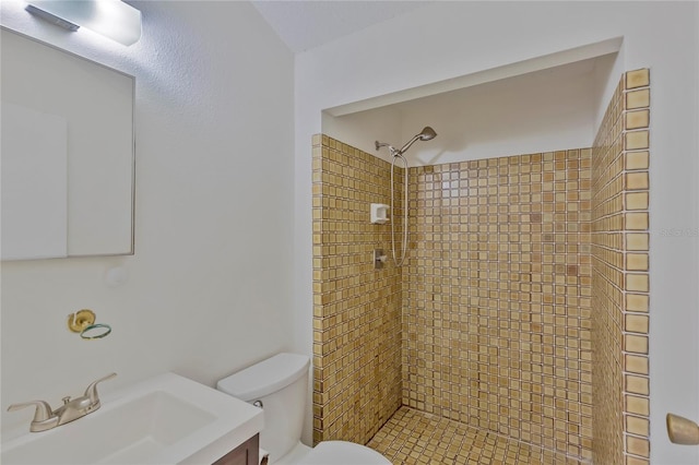 bathroom with a tile shower, vanity, and toilet