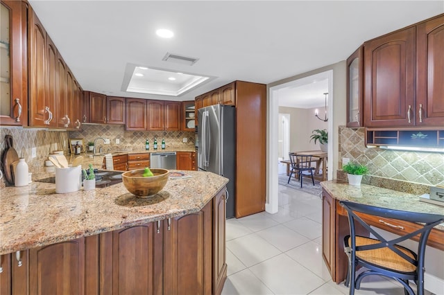 kitchen featuring light stone countertops, stainless steel appliances, light tile patterned floors, and a tray ceiling