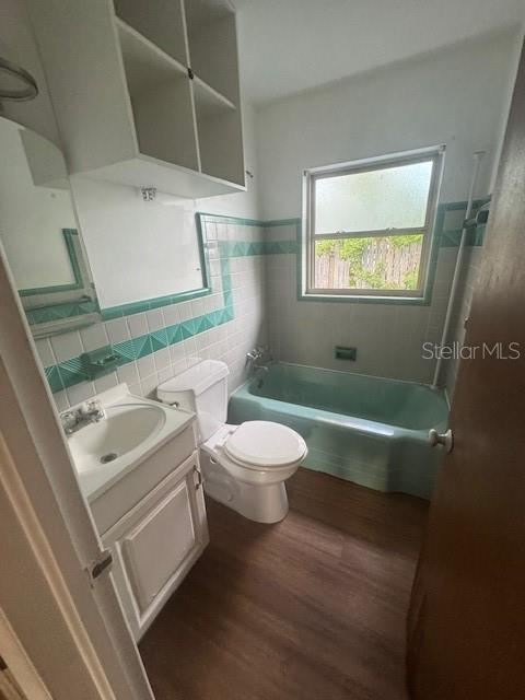 full bathroom featuring hardwood / wood-style floors, vanity, bathtub / shower combination, toilet, and tile walls