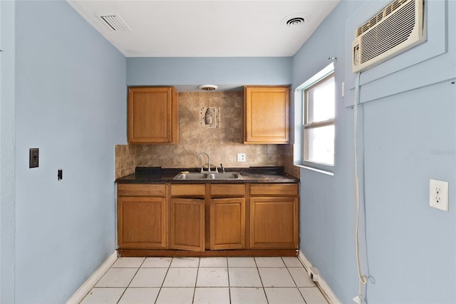 kitchen featuring a sink, backsplash, dark countertops, baseboards, and brown cabinetry