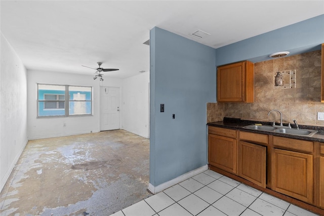 kitchen featuring a sink, brown cabinetry, dark countertops, a ceiling fan, and baseboards