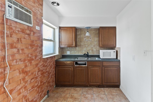 kitchen with a sink, white microwave, dark countertops, backsplash, and a wall unit AC