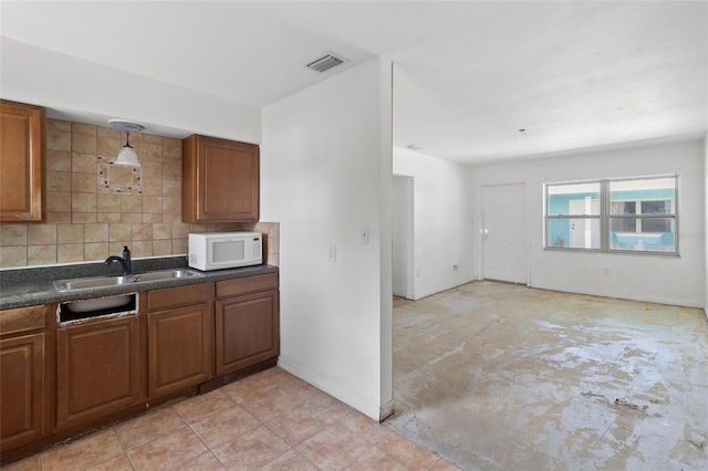 kitchen with white microwave, a sink, dark countertops, backsplash, and brown cabinetry