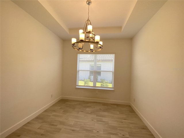 spare room with a raised ceiling, light hardwood / wood-style flooring, and a chandelier