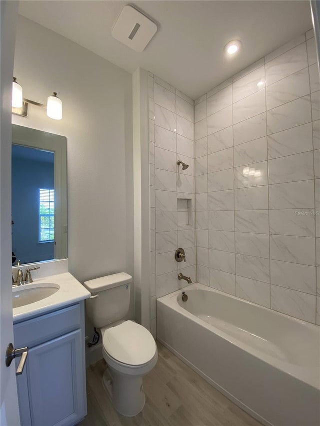 full bathroom featuring vanity, wood-type flooring, tiled shower / bath combo, and toilet