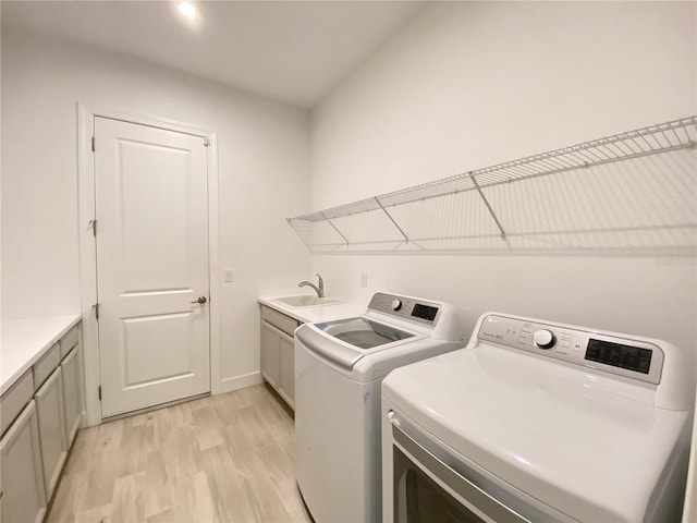 washroom featuring washing machine and clothes dryer, sink, cabinets, and light hardwood / wood-style flooring