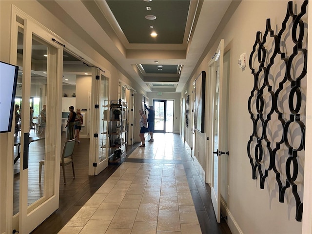 hall featuring french doors, light tile patterned floors, and a tray ceiling