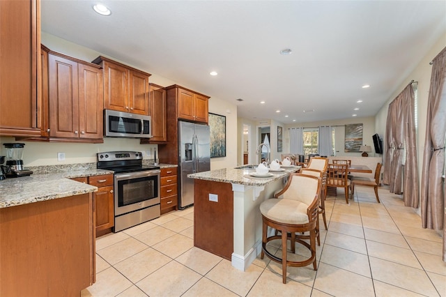 kitchen with a breakfast bar area, light stone countertops, a center island with sink, and stainless steel appliances