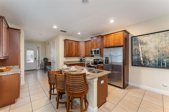 kitchen with a breakfast bar, stainless steel appliances, light stone counters, and light tile patterned flooring