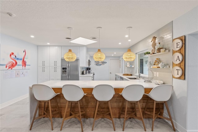 kitchen with a breakfast bar area, hanging light fixtures, stainless steel refrigerator with ice dispenser, sink, and white cabinetry