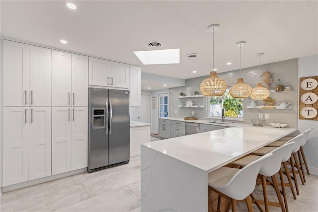 kitchen with pendant lighting, stainless steel appliances, a kitchen bar, white cabinetry, and sink