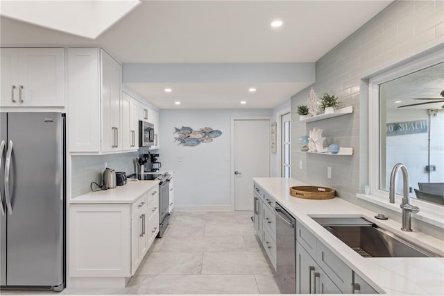 kitchen with light stone counters, tasteful backsplash, white cabinets, appliances with stainless steel finishes, and sink