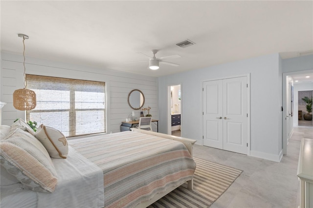 bedroom featuring ensuite bathroom, wood walls, ceiling fan, and a closet