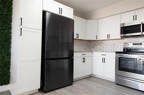 kitchen featuring stainless steel appliances, tasteful backsplash, white cabinets, and light wood-type flooring