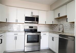 kitchen with sink, stainless steel appliances, light stone counters, white cabinets, and decorative backsplash