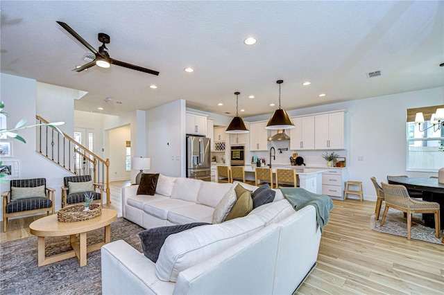 living room featuring a textured ceiling, light hardwood / wood-style flooring, ceiling fan with notable chandelier, and sink