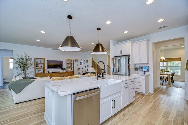 kitchen with a kitchen island with sink, white cabinets, sink, light wood-type flooring, and stainless steel appliances