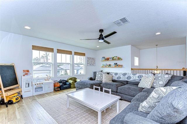 living room featuring ceiling fan with notable chandelier, a textured ceiling, and light hardwood / wood-style flooring