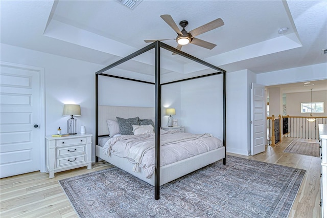 bedroom featuring a raised ceiling, ceiling fan, and light wood-type flooring