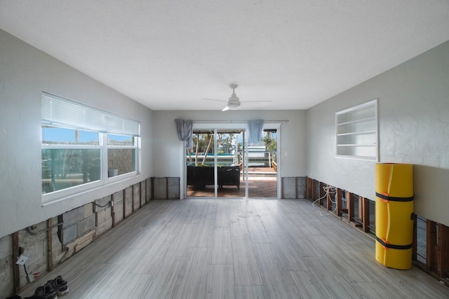 empty room featuring ceiling fan, light hardwood / wood-style flooring, built in features, and a textured ceiling